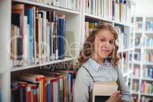 Portrait of happy schoolgirl holding book in library