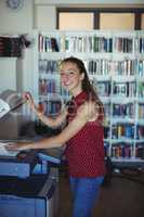 Portrait of happy schoolgirl using Xerox photocopier in library