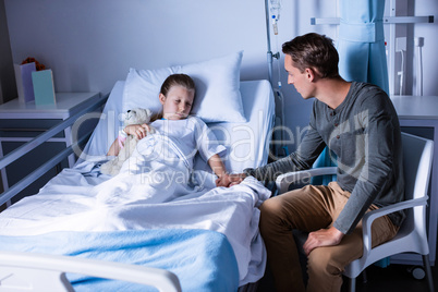 Father sitting beside her daughter lying on a hospital bed