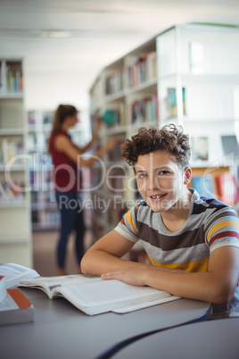 Portrait of happy schoolboy studying in library