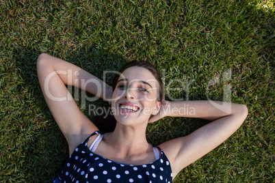Smiling woman lying on grass with hands behind head