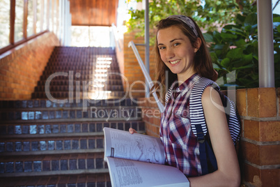 Portrait of schoolgirl reading book near staircase