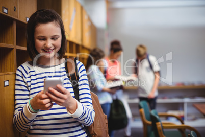 Happy schoolgirl using mobile phone in locker room