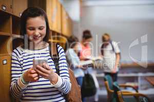 Happy schoolgirl using mobile phone in locker room