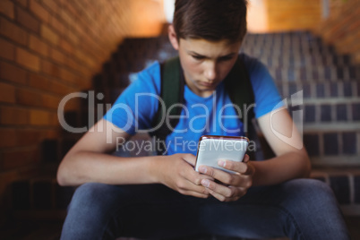Attentive schoolboy using mobile phone on staircase