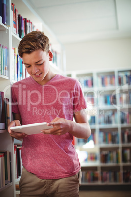 Happy schoolboy using digital tablet in library