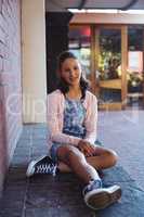 Happy schoolgirl sitting beside brick wall in school campus