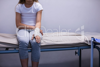 Girl with injured hand sitting on stretcher bed