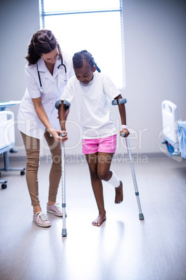 Female doctor assisting girl to walk with crutches in ward