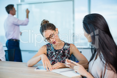 Smiling business colleagues writing on notepad and using digital tablet in conference room