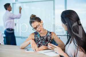 Smiling business colleagues writing on notepad and using digital tablet in conference room