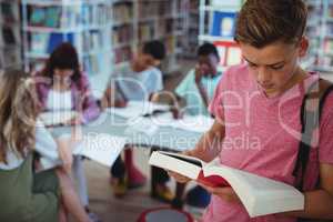 Schoolboy reading book with his classmates studying in background