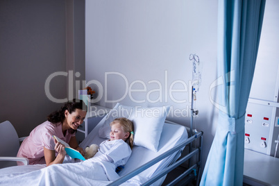 Girl on a hospital bed reading book with her mother