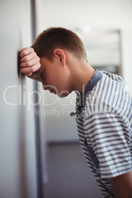 Sad schoolboy leaning head against wall in corridor