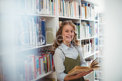 Portrait of happy schoolgirl reading book in library