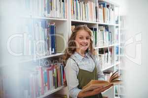 Portrait of happy schoolgirl reading book in library