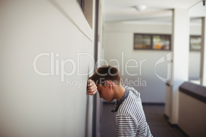 Sad schoolboy leaning head against wall in corridor