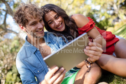 Couple sitting on grass and using digital tablet