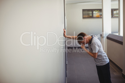 Sad schoolboy leaning against wall in corridor