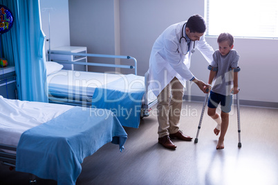 Doctor assisting injured boy to walk with crutches