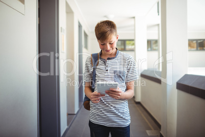 Happy schoolboy using digital tablet in corridor