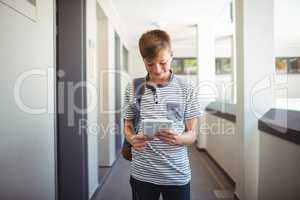 Happy schoolboy using digital tablet in corridor