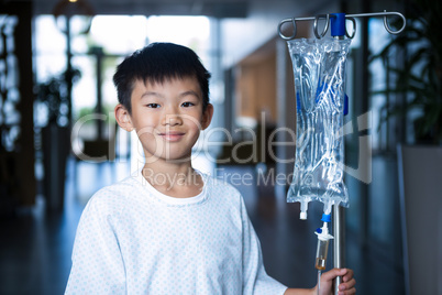 Smiling boy patient holding intravenous iv drip stand in corridor