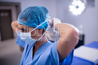 Female nurse tying surgical mask in operation theater