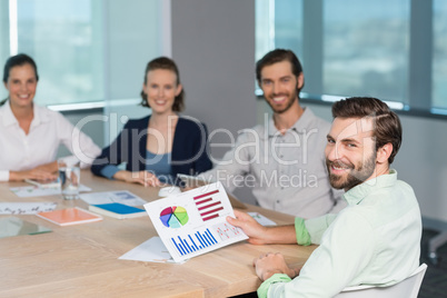 Smiling business executives sitting together in conference room with graph