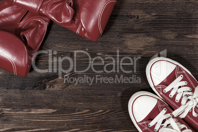 Red boxing gloves and red sneakers on a wooden surface