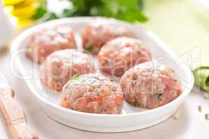 Raw meatballs on white plate, cooking in kitchen