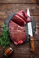 Raw liver on slate board on wooden background top view