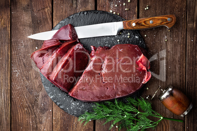 Raw liver on slate board on wooden background top view