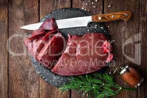 Raw liver on slate board on wooden background top view