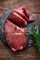 Raw liver on slate board on wooden background top view