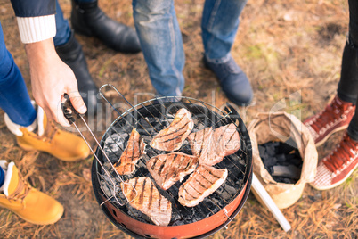 People cooking meat on charcoal grill