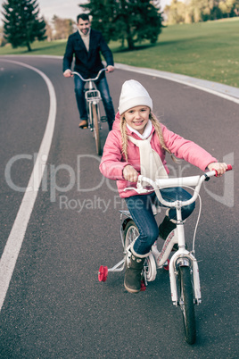 Smiling girl cycling with father