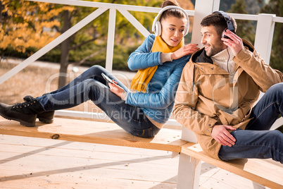 Young couple sitting on bench in headphones
