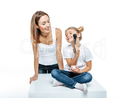 Mother looking at daughter with makeup brush