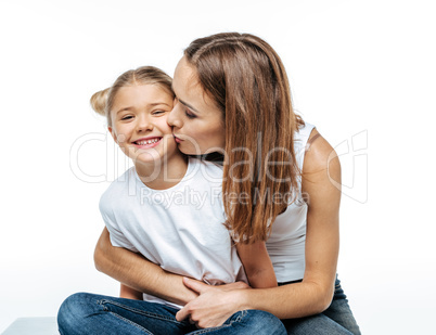 Mother hugging and kissing smiling daughter