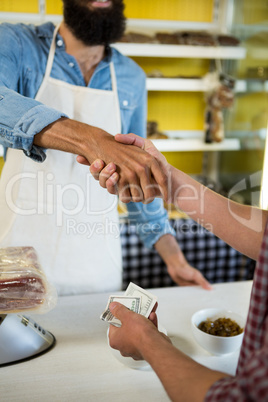 Mid section of staff and customer shaking hands at meat counter