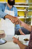 Mid section of staff and customer shaking hands at meat counter