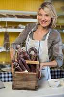 Portrait of female staff holding sausage in wooden basket at counter