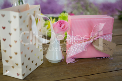 Gift bag, gift box and flower vase on wooden surface