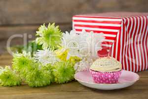 Gift box and flowers with cupcake in plate on wooden plank