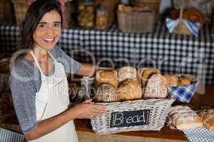 Female staff holding wicker basket of various breads at counter in bakery shop