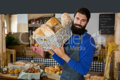 Portrait of male staff carrying wicker basket of breads at counter