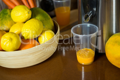 Lemons on wooden bowl with glass of juice at counter