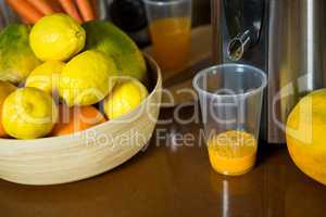 Lemons on wooden bowl with glass of juice at counter