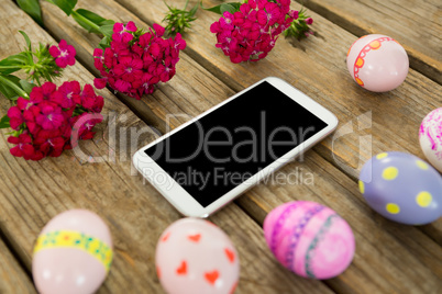 Painted Easter eggs, flowers and mobile phone on wooden surface